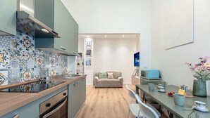 A compact kitchen with a tiled backsplash, a dining area with a table and chairs, and a sofa in the background. - [New Modern Apt.] Center 10 min • Hyper WiFi • A/C (Genoa)