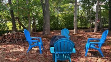 Three blue chairs arranged in a semi-circle facing a pile of logs and a building in the background.