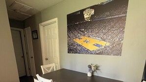 A dining area with a dark wooden table, white chairs, and a basketball court poster on the wall. - Ruppside Retreat I Cozy 2BR I 15m to RRG I Wi-Fi (Stanton)
