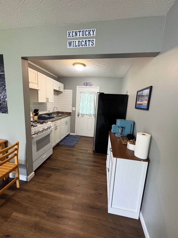 Una cucina con mobili bianchi, un frigorifero nero e un cartello con la scritta 'KENTUCKY WILDCATS'.