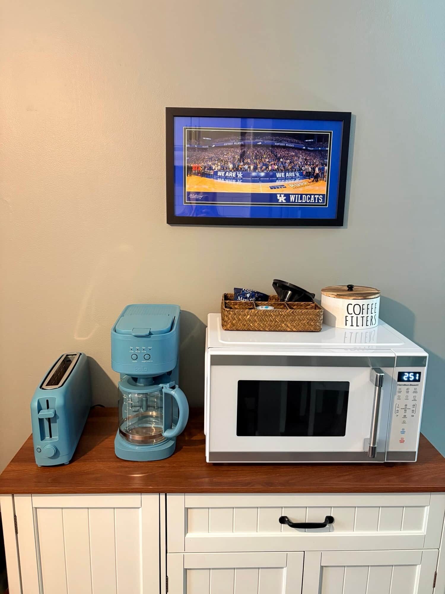 Uma bancada de cozinha com torradeira, máquina de café, micro-ondas e uma moldura com fotografia de um evento esportivo.
