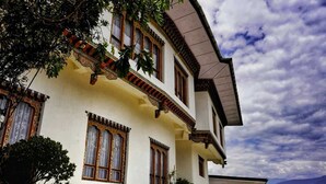 Un edificio tradicional con múltiples ventanas y balcones, rodeado de árboles y montañas al fondo.