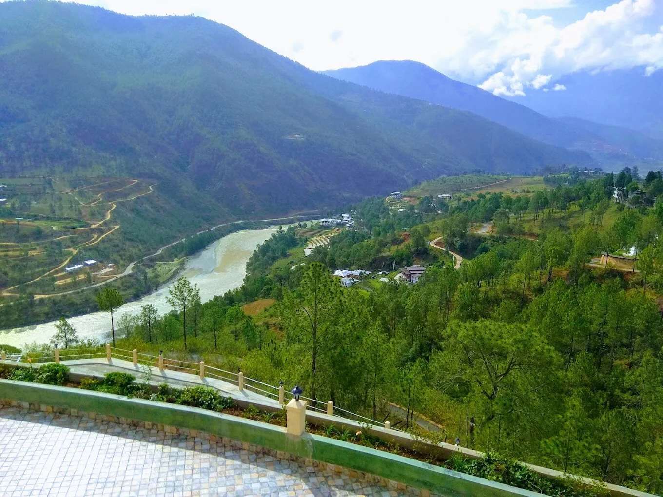 A mountainous landscape with a river, a bridge, and scattered buildings.
