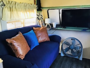 Ein blaues Sofa mit braunen Kissen, ein Standventilator und ein Fernseher auf einem Schrank.