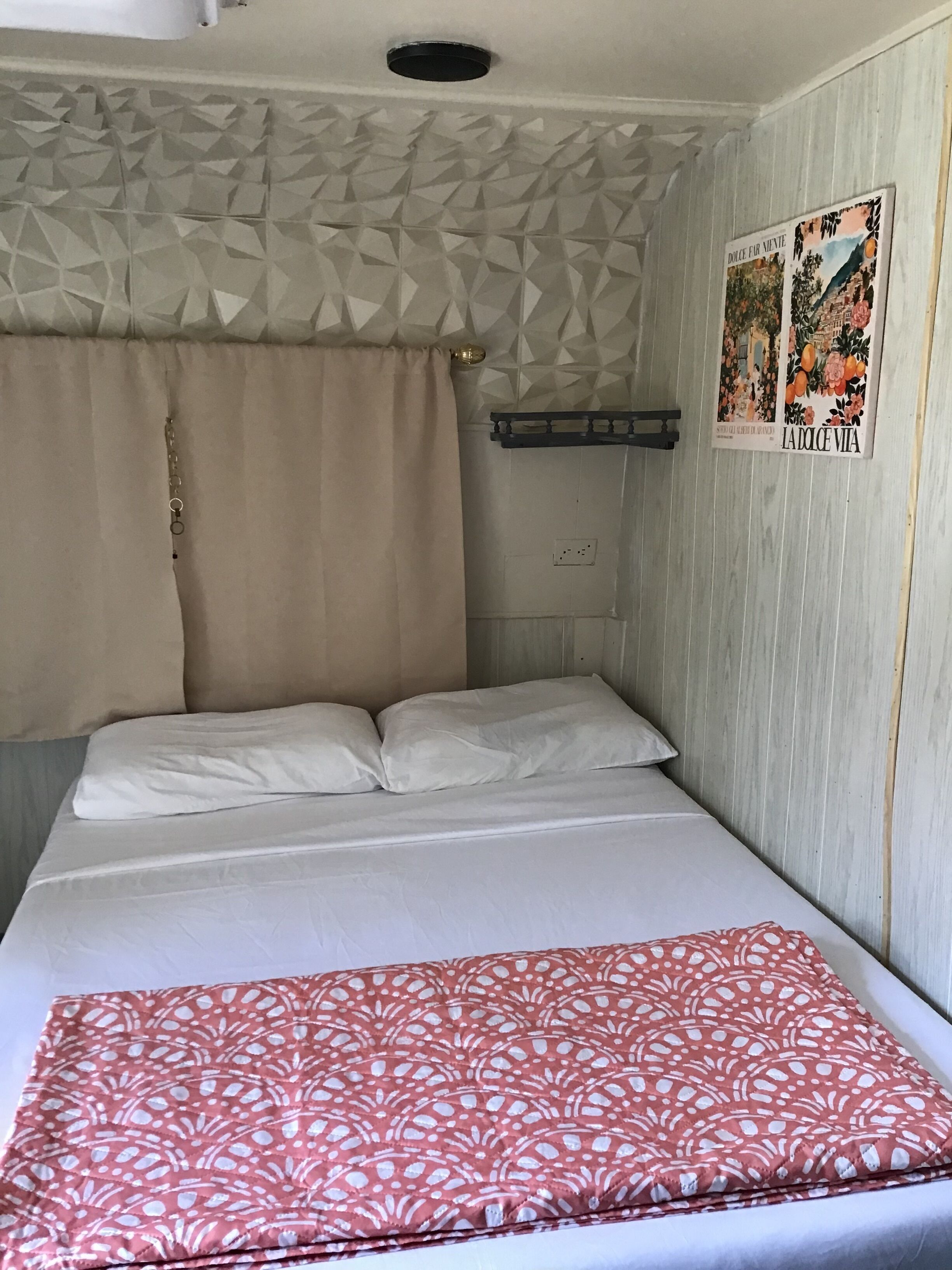 Ein Schlafzimmer mit einem Bett, einer gemusterten Decke, einem Vorhang und zwei Wandbildern.