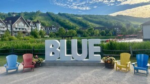 Un letrero con la palabra 'BLUE' en letras grandes, rodeado de sillas Adirondack en azul, rojo y amarillo.