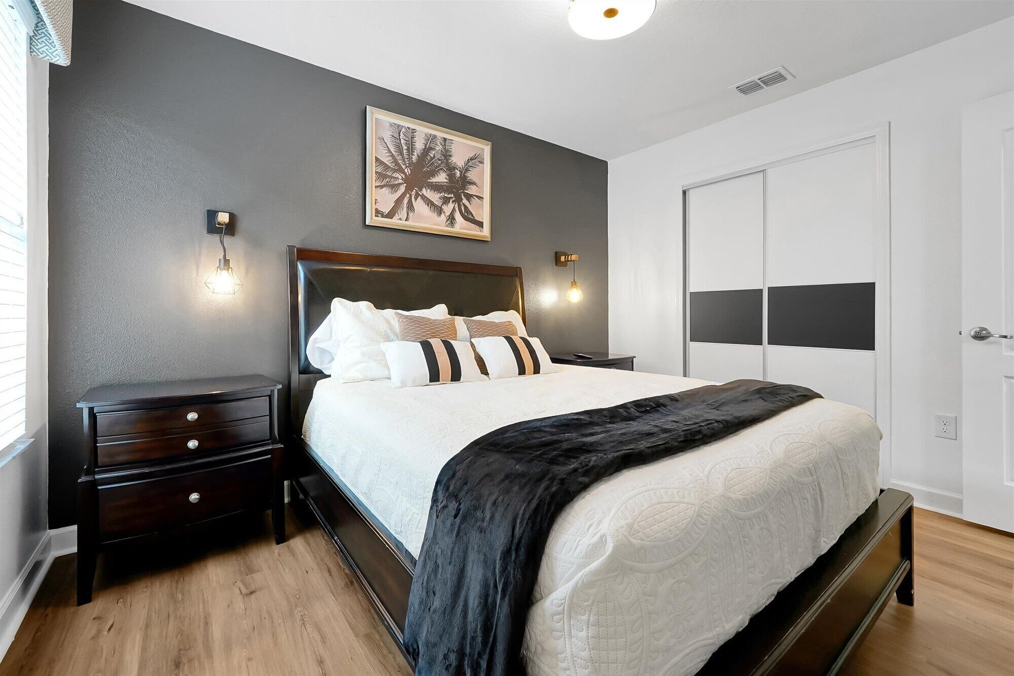 A bedroom with a bed, nightstands, a wall-mounted light, and a door.