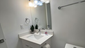 Ett badrum med ett vitt handfat, en spegel, en toalett och en hylla med växter.
