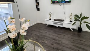 Ett modernt vardagsrum med en platt-TV som är monterad på väggen, ett vitt TV-bord och en krukväxt.