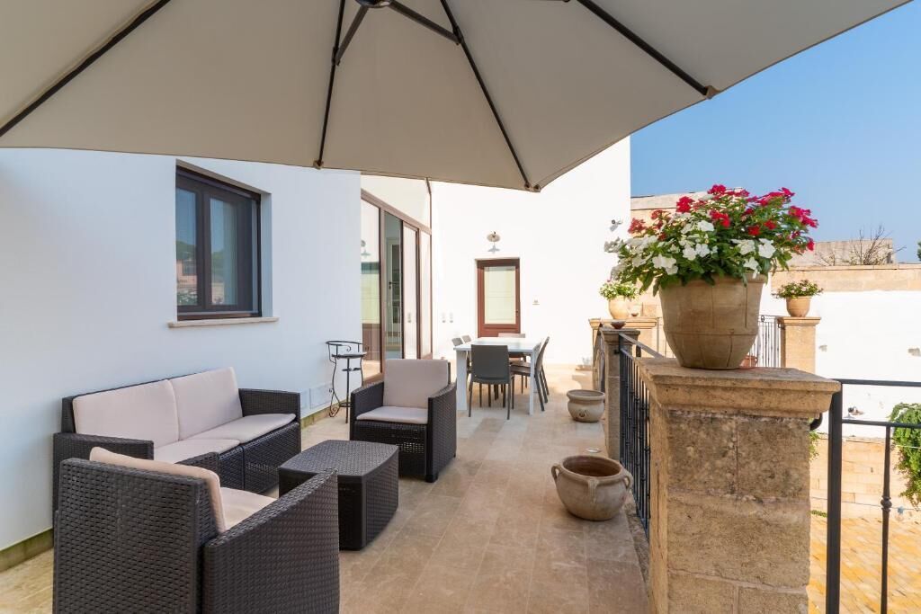 A balcony with wicker furniture, a table, chairs, a potted plant, and a stone pillar.