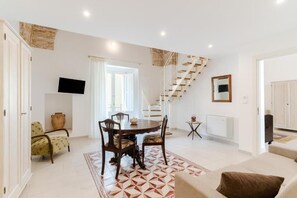 A spacious living area with a dining table, chairs, a sofa, a TV, a staircase, and a large window.