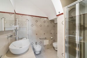 Un baño con un lavamanos grande de color blanco, un bidé, un inodoro y una zona de ducha con mampara de vidrio.