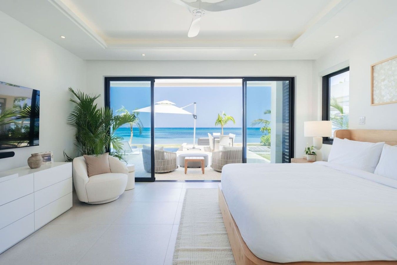 A modern hotel room with a large bed, a TV, a seating area with a view of the beach, and a sliding glass door leading to the outdoor space.