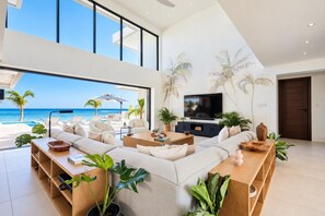 A modern living room with a large TV, comfortable seating, and a view of the ocean. - Beachfront 5BR Pool Villa | Private Chef, Butler | About Time Villa by Bocobay (St. Ann’s Bay)
