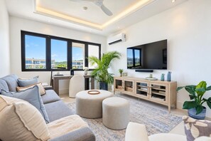 Ein modernes Wohnzimmer mit einer Couch, Hocker, einem Fernseher und einer Holzkommode.