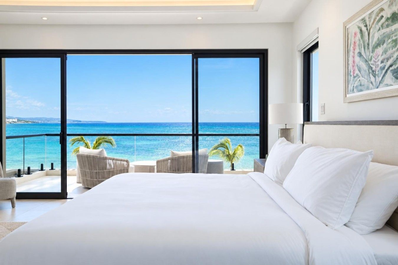Une chambre d’hôtel avec un grand lit, une vue sur l’océan et un balcon équipé de chaises.
