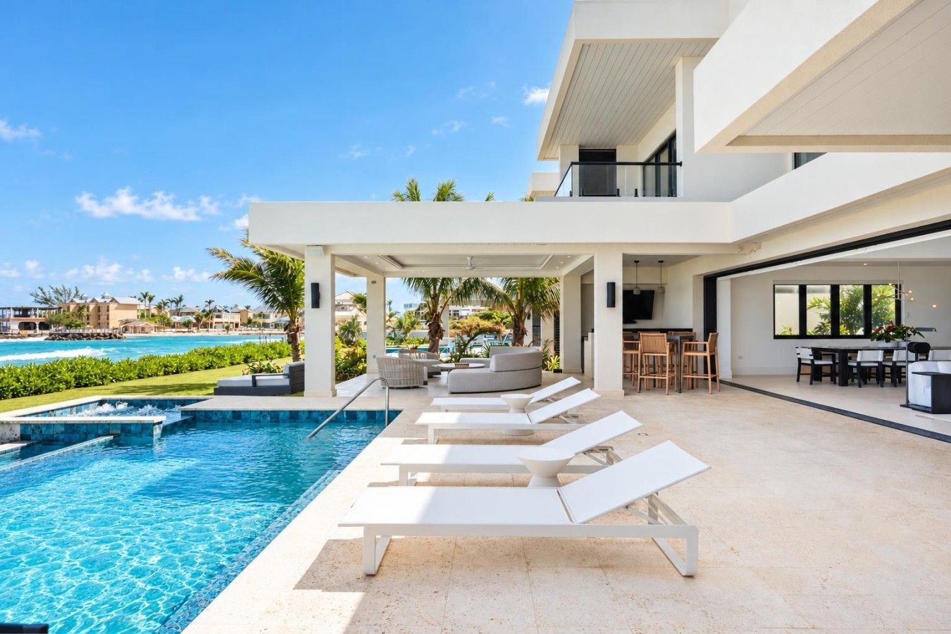 A modern outdoor pool area with lounge chairs, a dining area, and a view of the ocean.