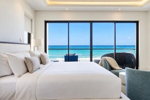 A hotel room with a large bed, a view of the ocean, and a seating area with a chair. - Ocean Front Staffed Villa | Lux Resort by Bocobay (St. Ann’s Bay)