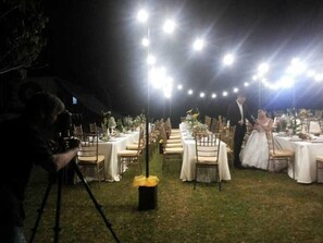 An outdoor wedding reception with tables set for guests, string lights overhead, and a photographer capturing the event. - THE Q Hotel Restaurant (Tagaytay)
