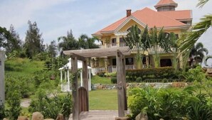 A large house with a red roof, a covered porch, and a garden with rocks and plants. - The Q Hotel Restaurant (Tagaytay)