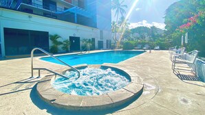 A swimming pool with a hot tub, lounge chairs, and a building with balconies. - Ocean-Front Condo•Semi-Private Beach•Pool•Hot Tub•Tennis.Free Parking. (Waianae)