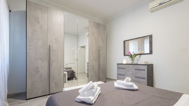 Une chambre d’hôtel moderne dotée d’un grand lit, d’une armoire avec un miroir, d’une coiffeuse avec un miroir et d’une salle de bain visible à travers une porte coulissante.