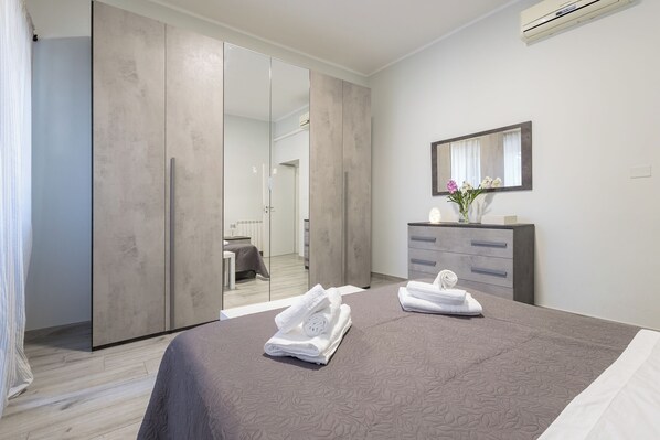 A modern hotel room with a large bed, a wardrobe with a mirror, a vanity with a mirror, and a bathroom visible through a sliding door. - Station House Ostia apartment with terrace, near sea and Rome (Lido di Ostia)
