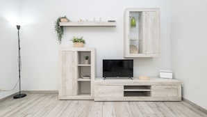 Un salon moderne doté d’un téléviseur à écran plat, d’un meuble de rangement en bois et d’une petite armoire surmontée d’une étagère.
