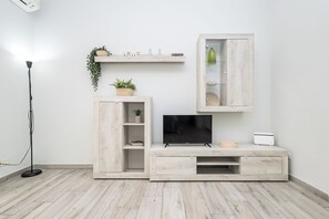 A modern living room with a flat-screen TV, wooden entertainment unit, and a small cabinet with a shelf above. - Station House Ostia apartment with terrace, near sea and Rome (Lido di Ostia)
