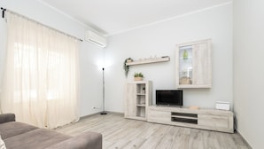 Un salon moderne avec un canapé, un téléviseur, un meuble en bois et une lampe sur pied.