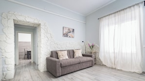 Une pièce avec un mur en pierre, un canapé gris, un rideau blanc et un tableau encadré accroché au mur.