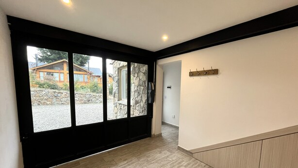Un intérieur spacieux avec une grande porte-fenêtre coulissante donnant sur un patio en pierre, un plancher en bois et un porte-manteau fixé au mur.