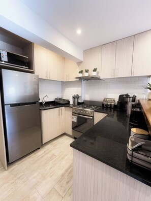 A modern kitchen with stainless steel appliances, light wood cabinets, and a black countertop.