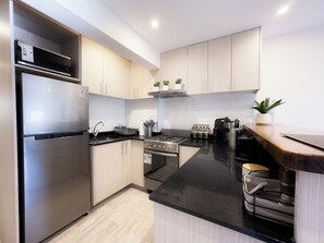 A modern kitchen with stainless steel appliances, wooden cabinets, and a black countertop.