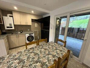 A compact kitchen with a built-in washing machine, a dining area with a patterned tablecloth, and a sliding glass door leading to an outdoor area.