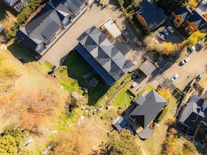 An aerial view of a residential area with multiple houses, a central building with a large roof, and a small pond.