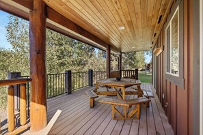 Een overdekt terras buiten met houten picknicktafels en banken, omgeven door een houten balustrade.