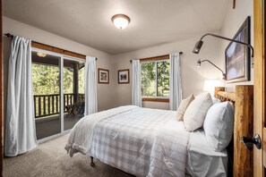 Een slaapkamer met een bed, een houten hoofdeinde, een plafondlamp en uitzicht op een terras.
