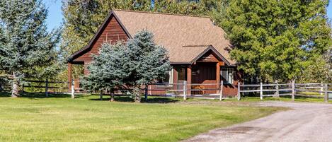A wooden cabin with a sloped roof, surrounded by a white fence, and a gravel path leading to it.