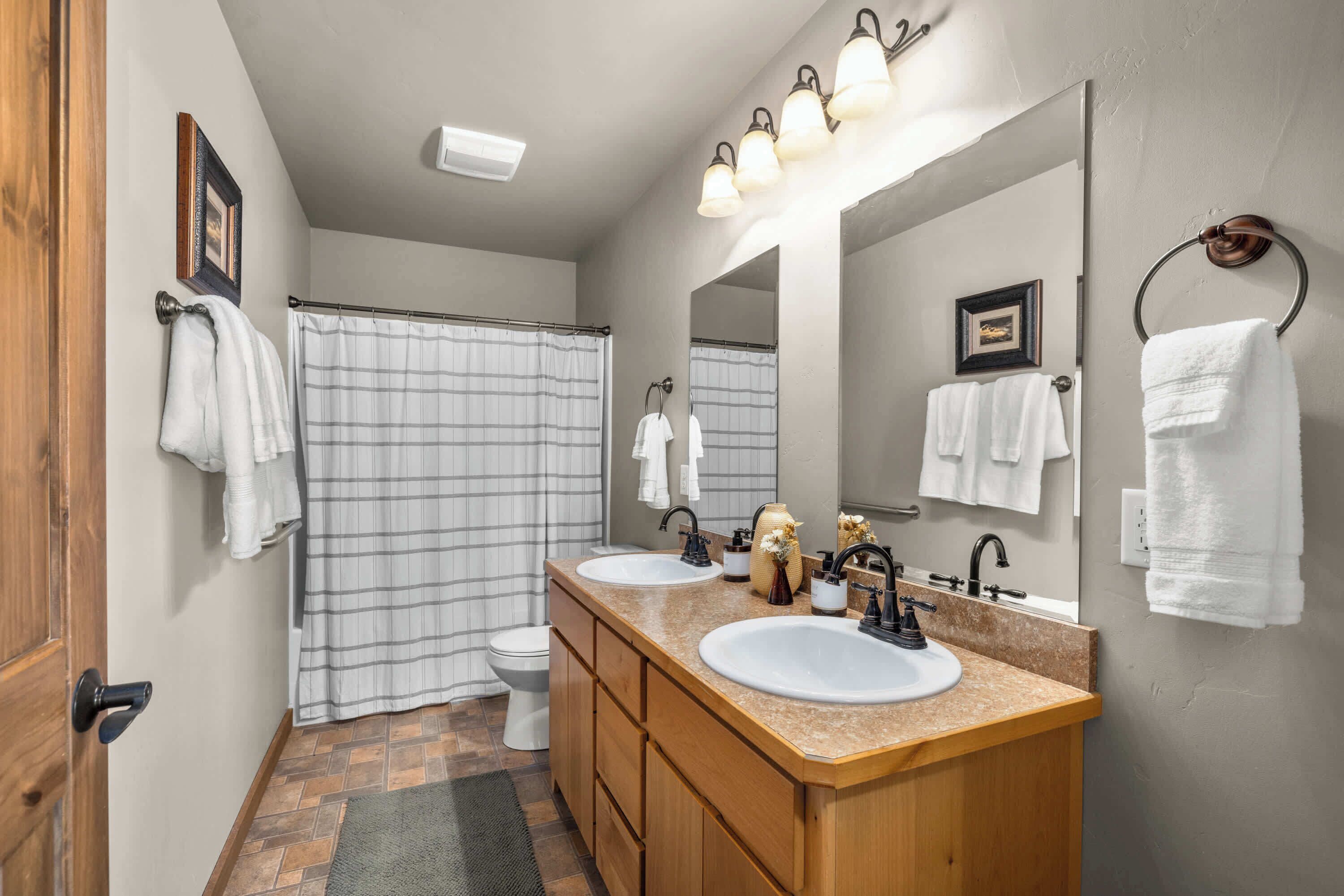 A bathroom with a shower, toilet, two sinks, a vanity, and a large mirror.