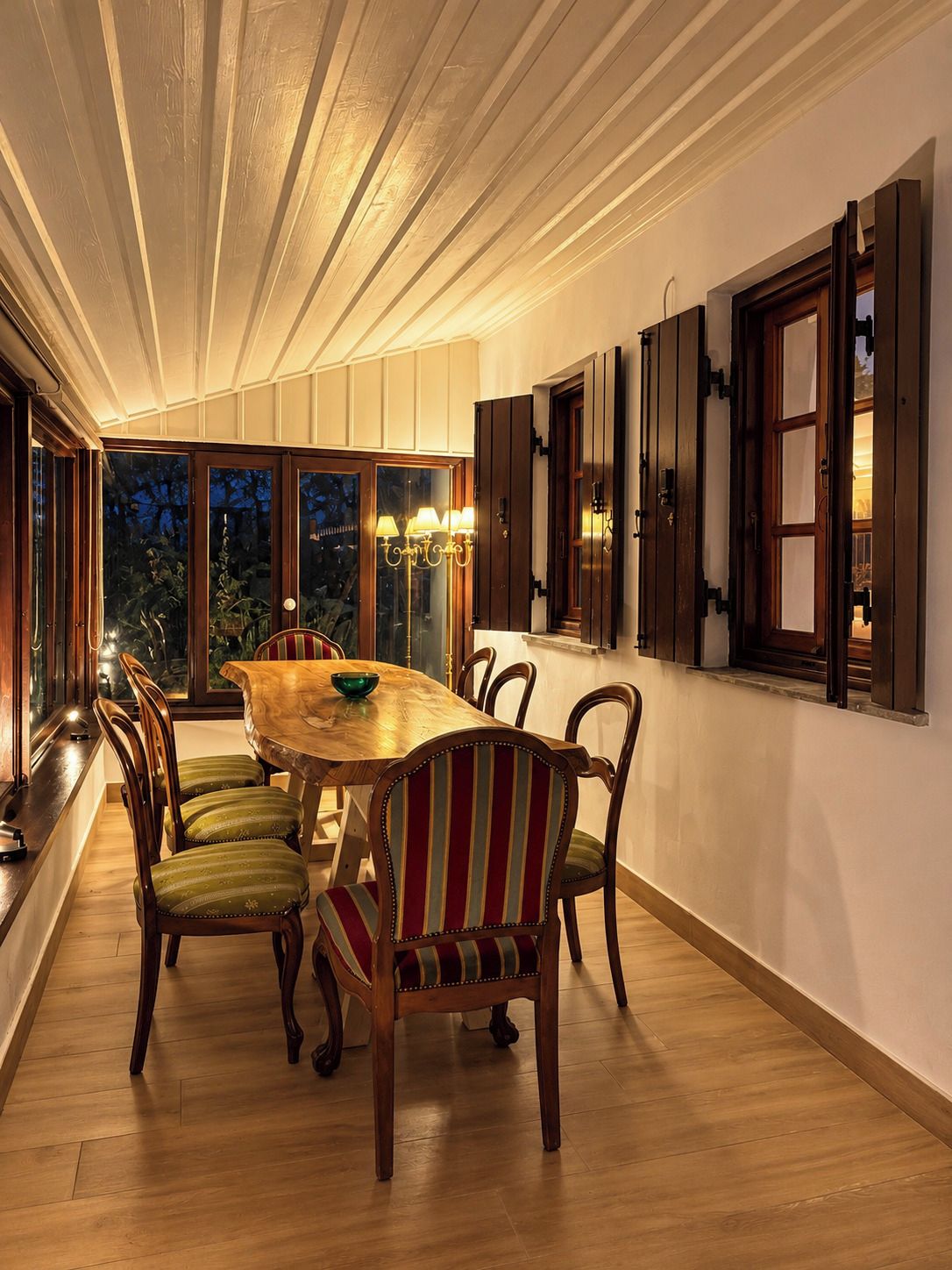 Un espace repas avec une table et des chaises en bois, un lustre et une vue dégagée grâce à de grandes fenêtres.