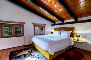 A bedroom with a wooden ceiling, a bed with white bedding, two windows, and a nightstand with a lamp.
