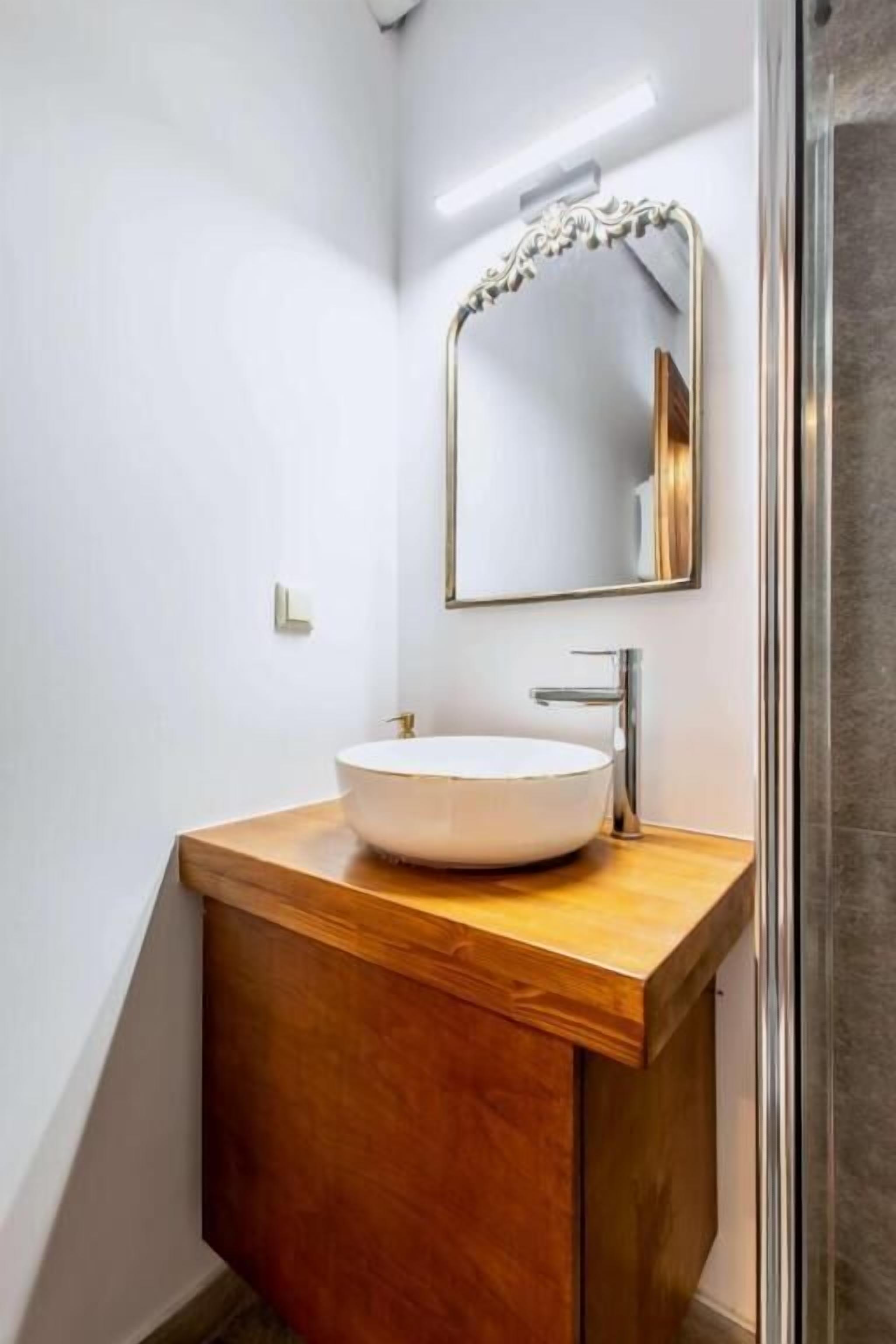 Ein modernes Badezimmer mit einem hölzernen Waschtisch, einem weißen Waschbecken und einem großen Spiegel.
