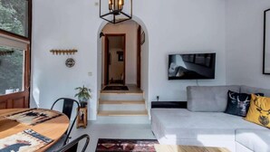 A living room with a sofa, a TV mounted on the wall, a dining table with chairs, and a staircase leading to another room. - MZ Reindeer (Distomo-Arachova-Antikyra)