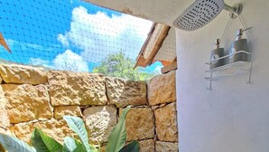 A shower area with a stone wall, a hanging showerhead, and a metal shelf with bottles.