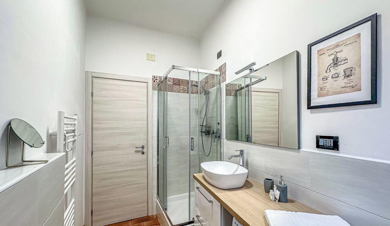 Un bagno moderno con cabina doccia in vetro, lavandino bianco e uno specchio grande.