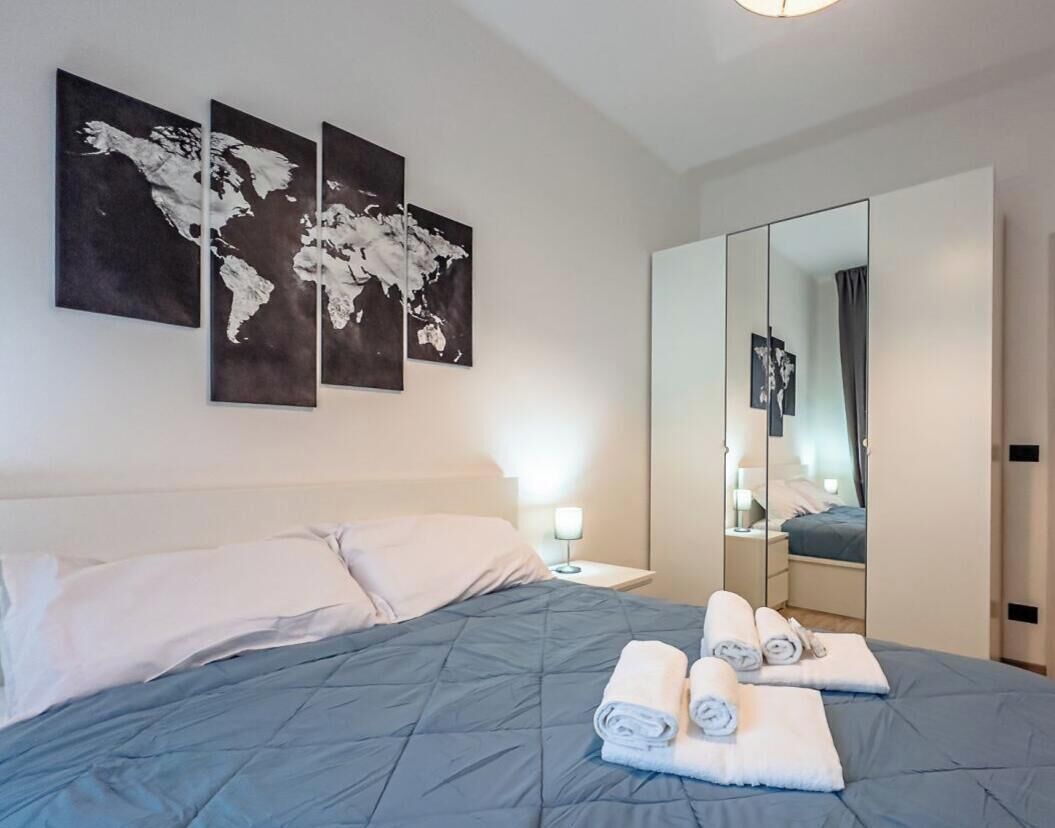 Ein Hotelzimmer mit einem Bett, einem Nachttisch, einem Spiegel und drei Weltkarten-Gemälden an der Wand.