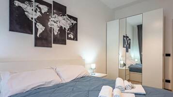 Ein Hotelzimmer mit einem Bett, einem Nachttisch, einem Spiegel und drei Weltkarten-Gemälden an der Wand.