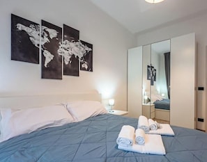 Una habitación de hotel con una cama, una mesita de noche, un espejo y tres cuadros con mapas del mundo en la pared.