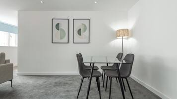 Un comedor moderno con una mesa de vidrio y cuatro sillas, una lámpara de pie y dos obras de arte abstracto en la pared.